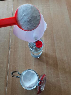 Ein weißliches Pulver wird mit einem Trichter in eine Plasteflasche mit Wasser abgefüllt