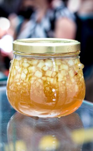 Ein Schraubglas mit Deckel, in dem sich eine gelbe Marmelade mit Apfelwürfel befindet.