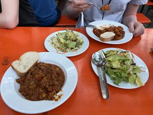 Jeweils 2 Teller mit Gulasch und Salat, auf einer Bierbank