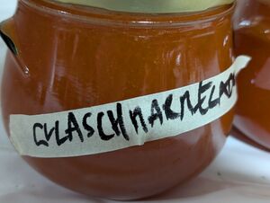 Ein Marmeladenglas mit einem rötlichen Inhalt, handbeschriftet auf einem Kreppapier mit dem Text GULASCHMARMELADE